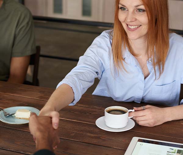 A white woman sitting at a table shakes hands with a Black man. 